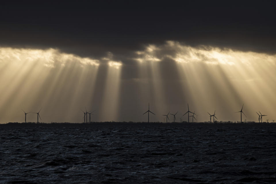 Sunlight breaks through dark clouds shining on a wind farm in Wilhelmshaven, on the North Sea coast of Germany, the evening of Sunday, Dec. 15, 2019. (Mohssen Assanimoghaddam/dpa via AP)