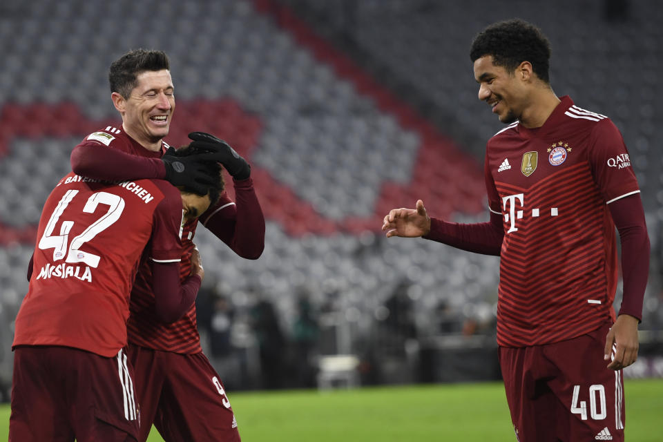 FILE - Bayern Munich's Robert Lewandowski, center, celebrates with teammates Jamal Musiala, left, and Malik Tillman, right, after scoring his side's fourth goal during a German Bundesliga soccer match against VfL Wolfsburg at the Allianz Arena in Munich, Germany, Dec. 17, 2021. Bayern Munich midfielder Tillman is switching affiliation from Germany to the United States and is among 27 players invited to the Americans’ next-to-last training camp ahead of the World Cup. (AP Photo/Andreas Schaad, File)