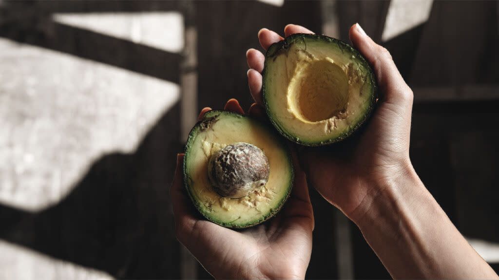 A man holds two halves of an avocado