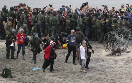 A police officer and a U.S. Customs and Border Protection (CBP) official detain people during a gathering in support of the migrant caravan in San Diego, U.S., close to the border wall between the United States and Mexico, as seen from Tijuana, Mexico December 10, 2018. REUTERS/Mohammed Salem