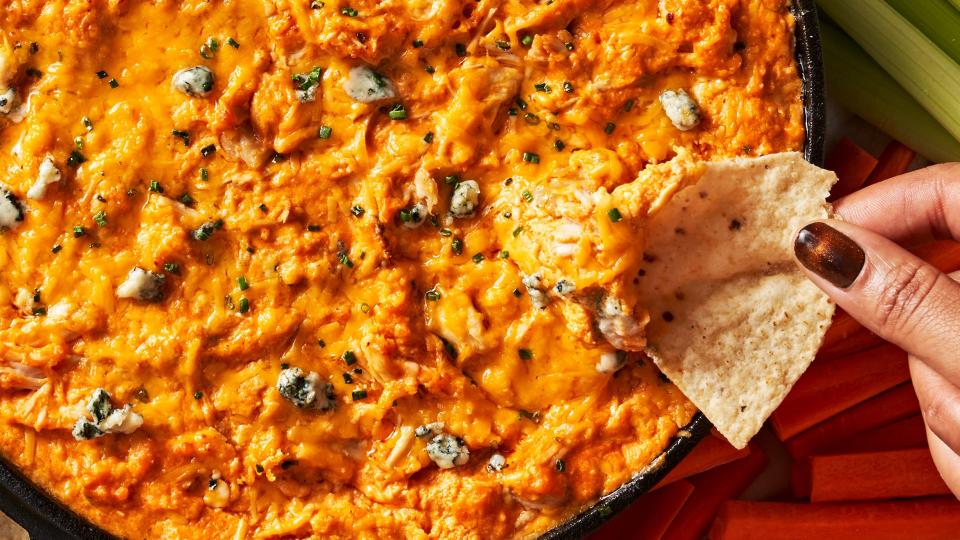 buffalo chicken dip in a skillet with celery and carrots beside and a tortilla chip dipping in