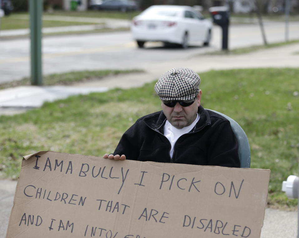 Edmond Aviv sits on a street corner holding a sign Sunday, April 13, 2014, in South Euclid, Ohio declaring he's a bully, a requirement of his sentence because he was accused of harassing a neighbor and her disabled children for the past 15 years. Municipal Court Judge Gayle Williams-Byers ordered Aviv, 62, to display the sign for five hours Sunday. It says: "I AM A BULLY! I pick on children that are disabled, and I am intolerant of those that are different from myself. My actions do not reflect an appreciation for the diverse South Euclid community that I live in." (AP Photo/Tony Dejak)