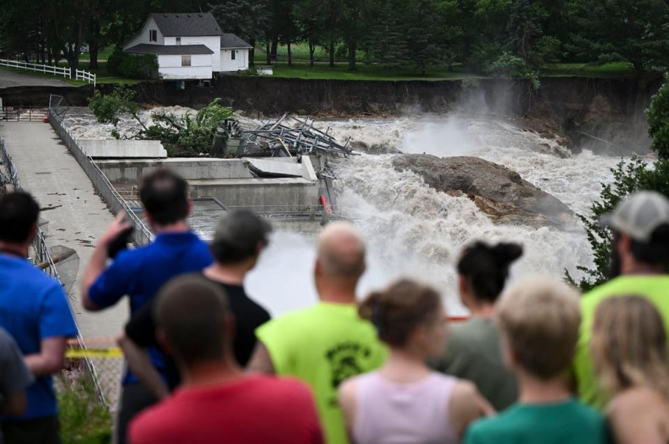 A crowd watches a home on the brink of collapse near the Rapidan Dam in Minnesota. Severe flooding and debris caused the dam to partially fail on Monday (AP)