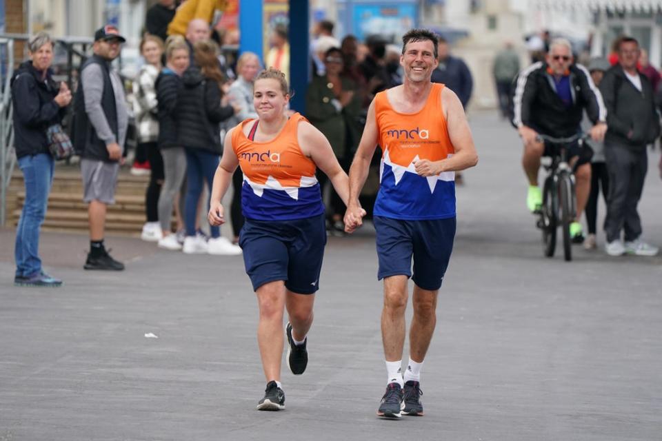 Charlotte Nichols and Stuart Bates hold hands as they run towards the finish line of their marathon at Weymouth Beach (Andrew Matthews/PA) (PA Wire)