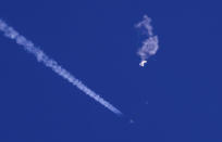 In this photo provided by Chad Fish, the remnants of a large balloon drift above the Atlantic Ocean, just off the coast of South Carolina, with a fighter jet and its contrail seen below it, Saturday, Feb. 4, 2023. The downing of the suspected Chinese spy balloon by a missile from an F-22 fighter jet created a spectacle over one of the state's tourism hubs and drew crowds reacting with a mixture of bewildered gazing, distress and cheering. (Chad Fish via AP)