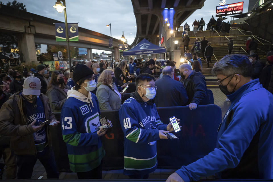 A fan shows his vaccine passport on his phone and identification before entering Rogers Arena for the Vancouver Canucks NHL hockey game against the Minnesota Wild in Vancouver, British Columbia on Tuesday, Oct. 26, 2021. The home opener is the team's first home game with capacity restrictions lifted for fans since the COVID-19 pandemic forced the NHL to halt last season in March, 2020. (Darryl Dyck/The Canadian Press via AP)