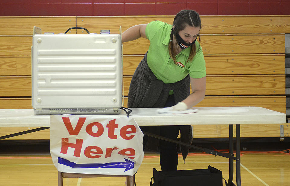 Volunteer Mackenzie McKee wipes down a voting table in preparation for the primary election, in the Terre Haute South High School auxiliary gym, Tuesday, June 2, 2020, in Terre Haute, Ind. (Joseph C. Garza/Tribune-Star via AP)