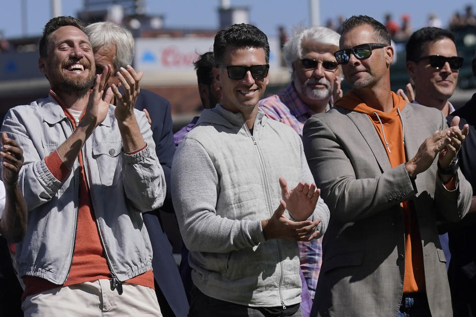 Former San Francisco Giants players Hunter Pence, Buster Posey and Ryan Vogelsong, from left in front, applaud during a ceremony inducting longtime clubhouse manager Mike "Murph" Murphy into the team's Wall of Fame before a baseball game between the Giants and the Atlanta Braves in San Francisco, Sunday, Aug. 27, 2023. Posey has a year's worth of coursework remaining to complete his degree in social science at Florida State, yet he plans to spend the next two years finishing up given his busy home life with four children. (AP Photo/Jeff Chiu)