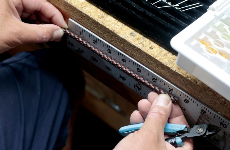 Paul Rudy, 56, of St. Clair Shores, at his work area in his basement on Wednesday, Aug. 23, 2023, measures the length of a leather bracelet he was making, one of a variety of items he creates here, including earrings and eyeglass straps. His De Suave line of straps are popular on Amazon, Etsy and they are for sale at Eastern Market in Detroit as well.