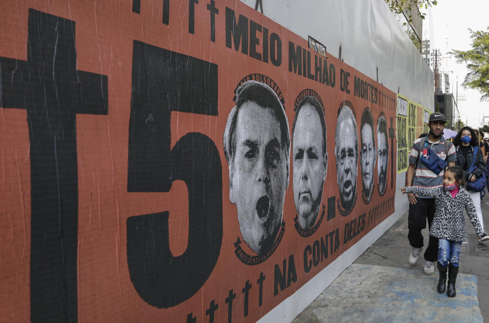 A girl points at a mural featuring the face of Brazilian President Jair Bolsonaro during a protest against his handling of the COVID-19 pandemic along Paulista Avenue, in Sao Paulo, Brazil, Saturday, June 19, 2021. Brazil's COVID-19 death toll is expected to surpass the milestone of 500,000 deaths on Saturday night. (AP Photo/Marcelo Chello)