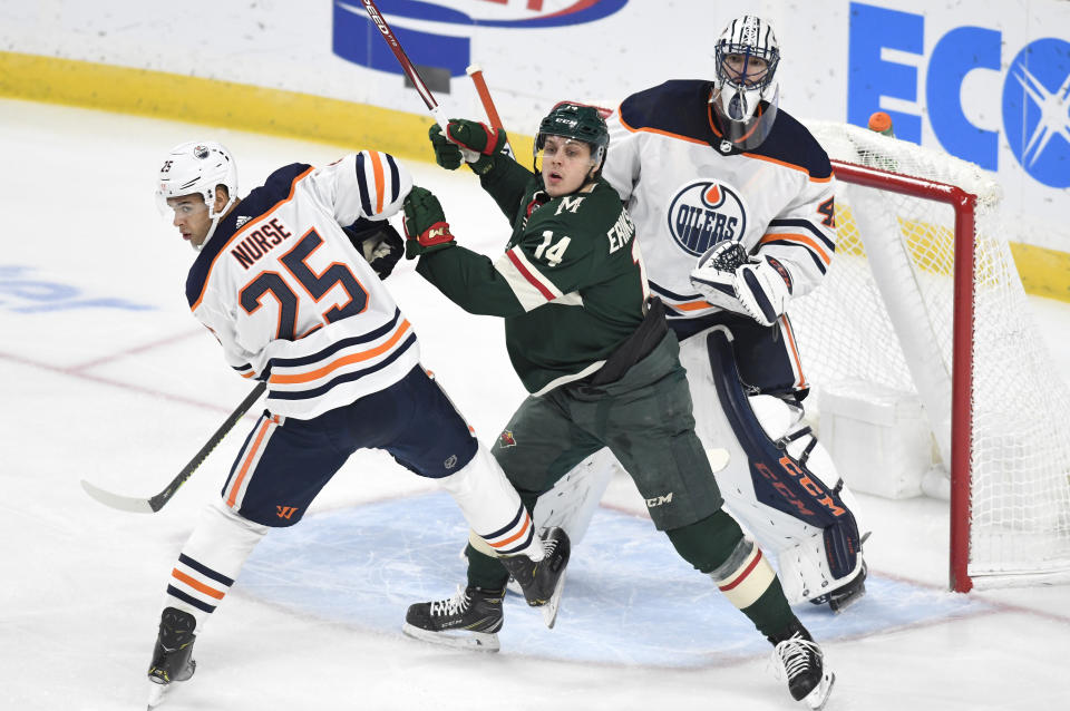 Edmonton Oilers goalie Mike Smith, right, looks over teammate Darnell Nurse (25) and Minnesota Wild's Joel Eriksson Ek, center, of Sweden, for the puck in the first period of an NHL hockey game, Thursday, Dec.12, 2019, in St. Paul, Minn. (AP Photo/Tom Olmscheid)