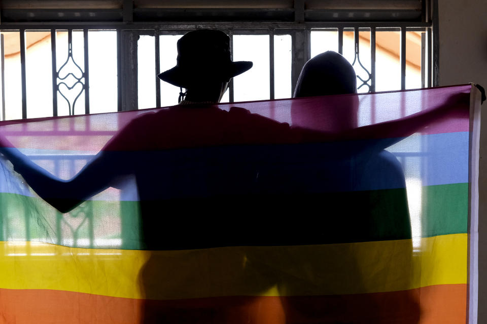 A gay Ugandan couple cover themselves with a pride flag as they pose for a photograph in Uganda Saturday, March 25, 2023. A prominent leader of Uganda's LGBTQ community on Thursday described anguished calls by others like him who are concerned for their safety after the passing of a harsh new anti-gay bill. (AP Photo)