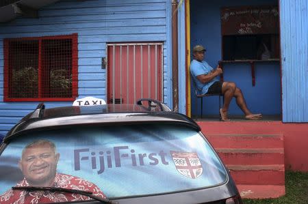 An election poster for Voreqe "Frank" Bainimarama can be seen in the rear window of a taxi as a man gestures from the doorway of a local gymnasium in the Fiji capital of Suva August 26, 2014. REUTERS/Lincoln Feast