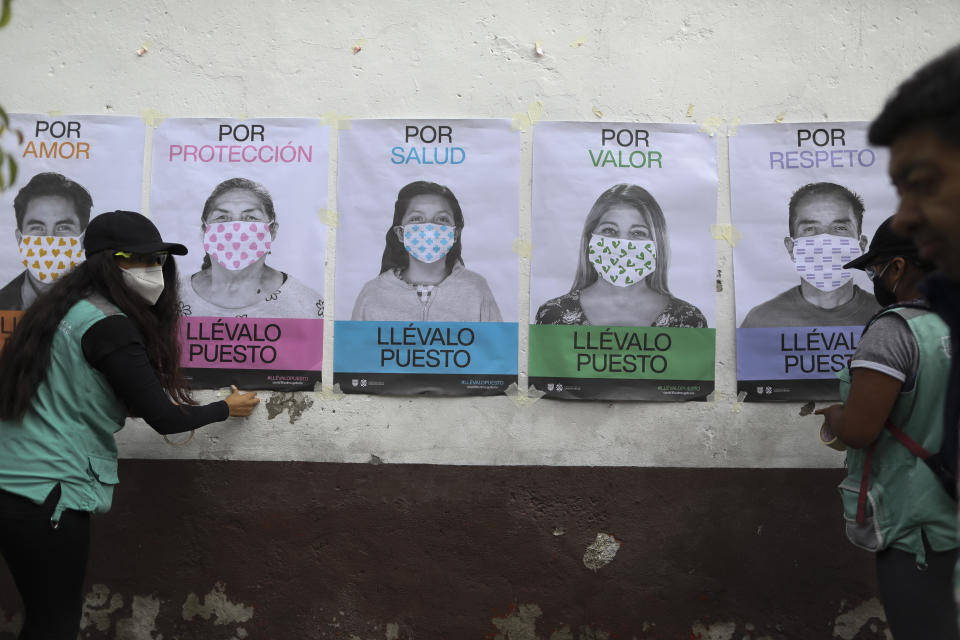 A man not wearing a face mask walks by as city health department workers affix a series of posters advocating mask use to a wall, in San Mateo Xalpa in the Xochimilco district of Mexico City, Tuesday, July 21, 2020. The posters say, in Spanish, "For love, for protection, for health, for self-worth, for respect, wear it." To help battle the pandemic in hard-hit areas, the city health department has set up mobile testing units and sent teams of workers to hang posters and distribute informational pamphlets about how to prevent tCOVID-19. (AP Photo/Rebecca Blackwell)