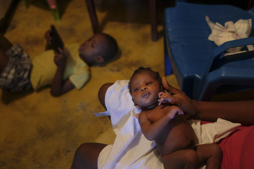 Veronique Louis holds her daughter as her son plays with a cell phone in her home in the Los Coquitos neighborhood of Santo Domingo, Dominican Republic, Sunday, Nov. 21, 2021. Earlier this month, Louis gave birth to her daughter at a hospital in Santo Domingo. She returned days later for further treatment because they botched the cesarean, but medical staff denied her care, according to her husband, Wilner Rafael. “They said they weren’t treating Blacks, and that Haitians aren’t people,” he said. (AP Photo/Matias Delacroix)