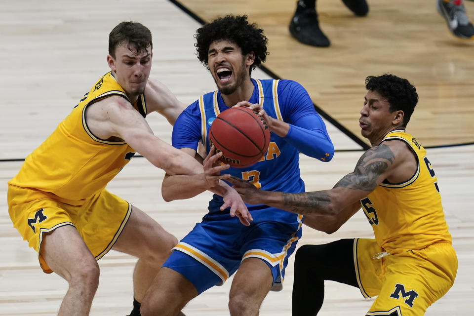 UCLA guard Johnny Juzang is fouled while catching a pass between Michigan guard Franz Wagner, left, and guard Eli Brooks, right, during the second half of an Elite 8 game in the NCAA men's college basketball tournament at Lucas Oil Stadium, Tuesday, March 30, 2021, in Indianapolis. (AP Photo/Michael Conroy)