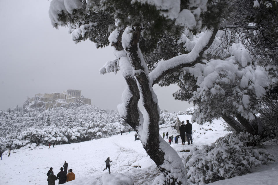People play in the snow at Filopapos Hill in front the ancient Acropolis hill with the ruins of the fifth century B.C. Parthenon temple, in Athens, on Tuesday, Feb. 16, 2021. Unusually heavy snowfall has blanketed central Athens, with authorities warning residents particularly in the Greek capital's northern and eastern suburbs to avoid leaving their homes. (AP Photo/Petros Giannakouris)