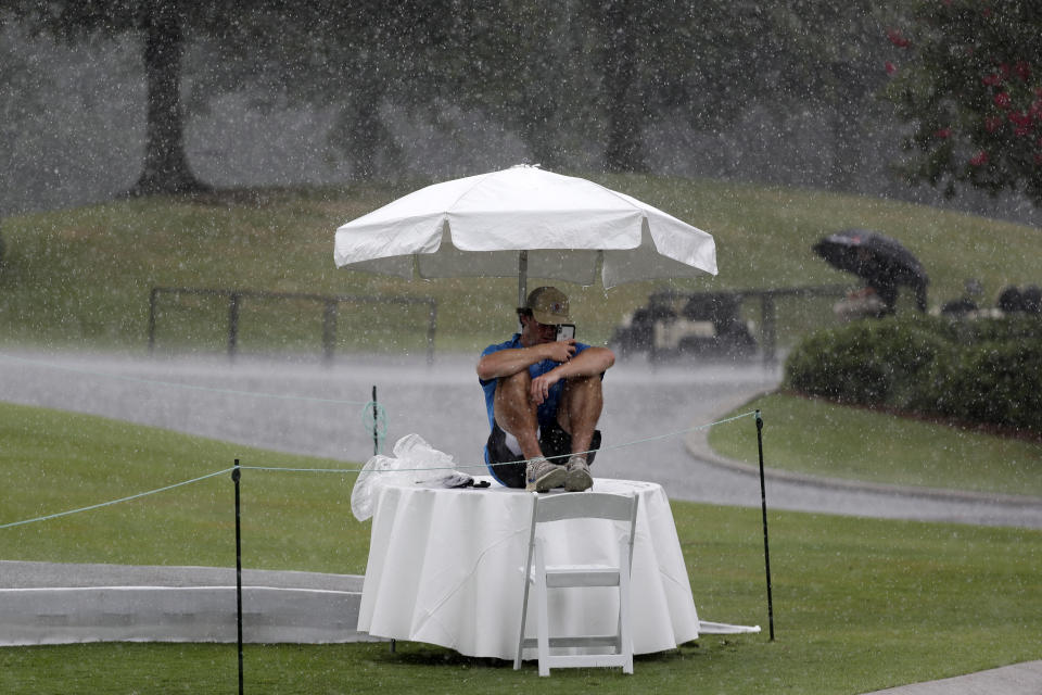 Security worker Raymond Fracchia takes shelter under an umbrella as rain falls during a practice round at the World Golf Championship-FedEx St. Jude Invitational Wednesday, July 29, 2020, in Memphis, Tenn. (AP Photo/Mark Humphrey)