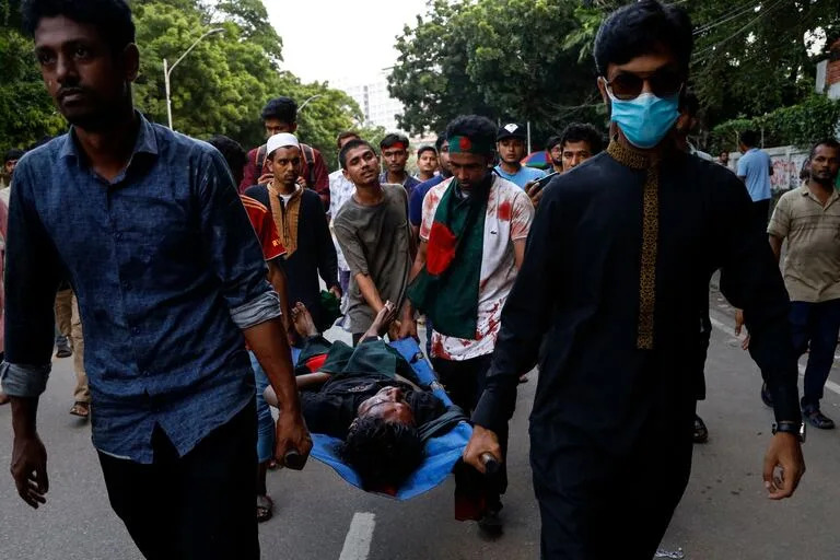 Manifestantes llevan el cuerpo de un estudiante mientras marchan por una calle para protestar en Dhaka.