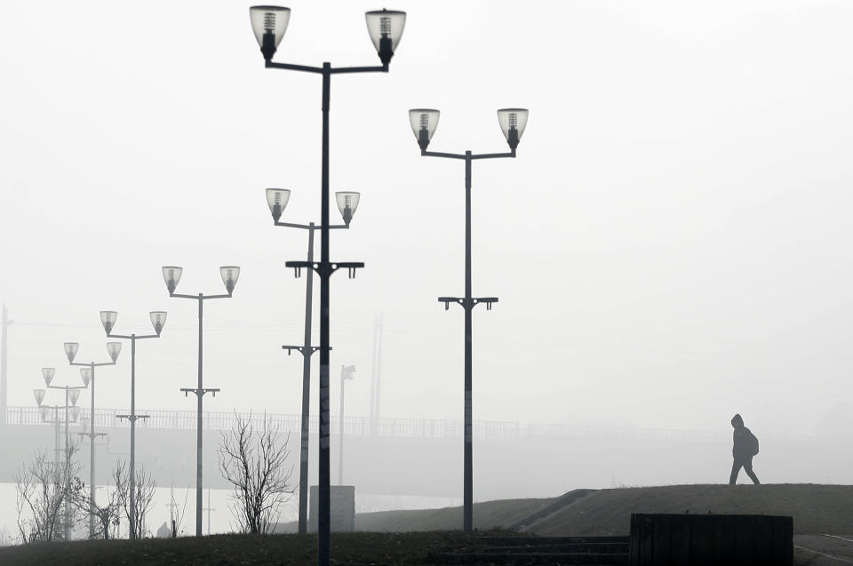 A man walks on the bank of Sava river in Belgrade, Serbia, Wednesday, Jan. 15, 2020. Serbia's government on Wednesday called an emergency meeting, as many cities throughout the Balkans have been hit by dangerous levels of air pollution in recent days, prompting residents' anger and government warnings to stay indoors and avoid physical activity. (AP Photo/Darko Vojinovic)