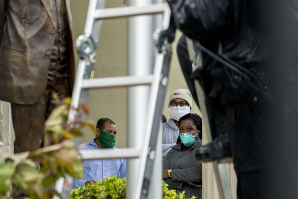 People with the Cuban Embassy wear masks due to the Coronavirus outbreak as they watch Secret Service investigators examine bullet holes in front of the Cuban Embassy after police say a person with an assault rifle opened fire, Thursday, April 30, 2020, in Washington. (AP Photo/Andrew Harnik)