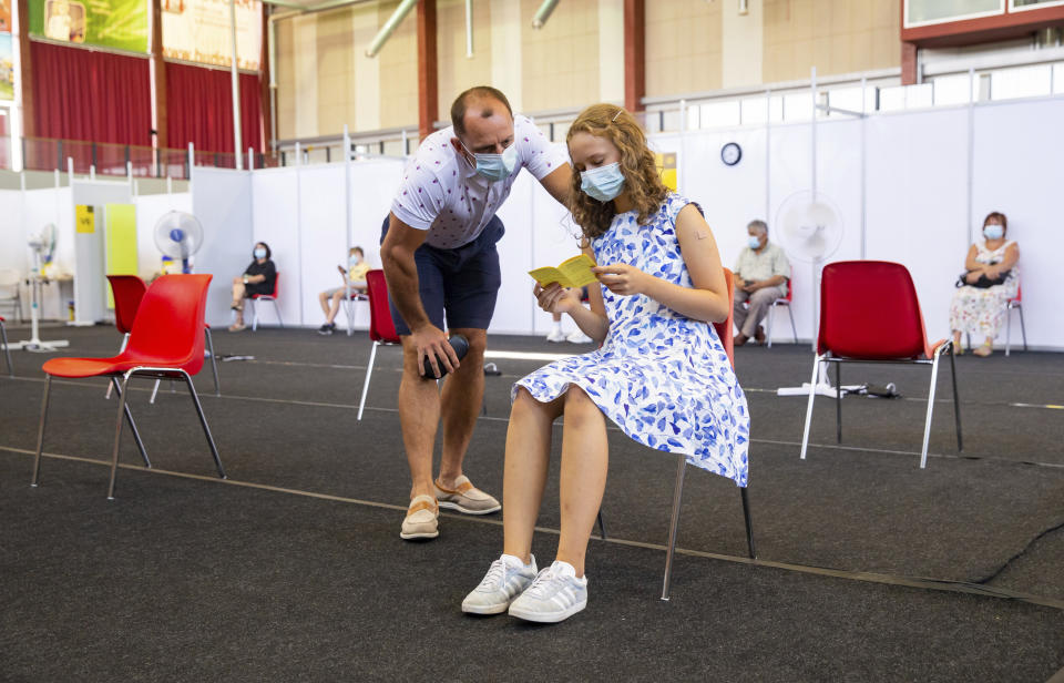 Gloria Raudjarv, 13-year-old girl, reads her vaccination certificate after getting an injection as her father Ivo, speaks to her at a vaccination center inside a sports hall in Estonia's second largest city, Tartu, 164 km. south-east from Tallinn, Estonia, Thursday, July 29, 2021. Estonia's second largest city Tartu is making rapid progress in vaccinating children aged 12-17 ahead of the school year in September. Around half of the town's teenagers have already received their first vaccine, and local health officials are confident they will hit 70% in the coming 30 days. (AP Photo/Raul Mee)