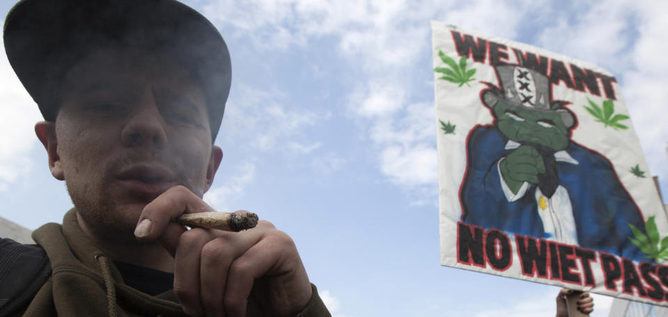 FILE - In this Friday April 20, 2012 file photo a man smokes a marijuana joint during a protest against a government plan to stop foreigners from buying marijuana in the Netherlands. The new Dutch government is scrapping a planned "weed pass" designed to keep foreigners out of the nation's cannabis-selling coffee shops. Justice Minister Ivo Opstelten said late Monday, Nov. 19, 2012 that the passes are being immediately scrapped. Placard reads: "We Want No Weed Pass". (AP Photo/Peter Dejong, File)