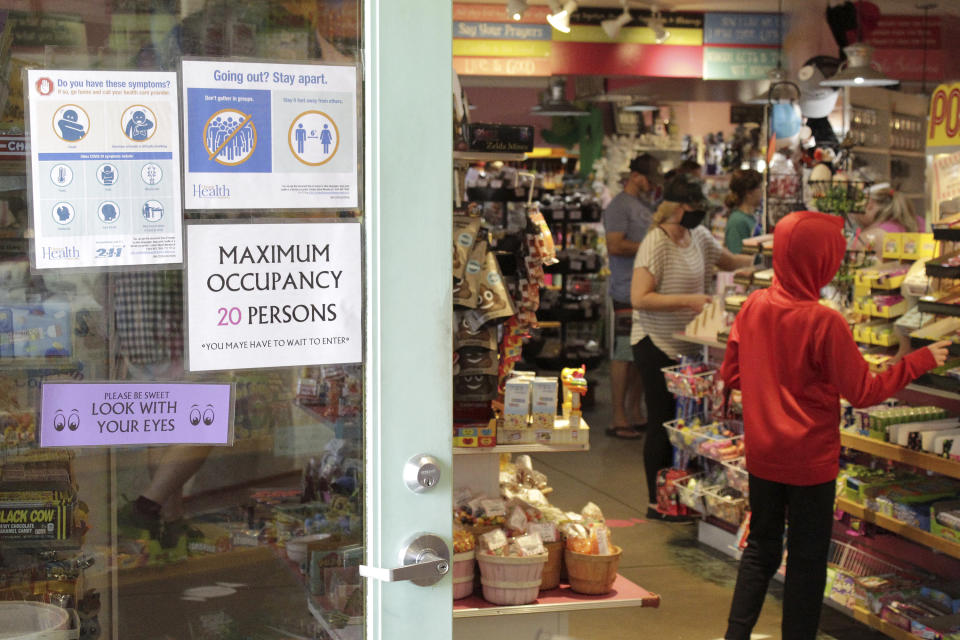In this Thursday, May 28, 2020, photo tourists shop at Bruce's Candy Kitchen amid social distancing restrictions during the coronavirus outbreak in Cannon Beach, Ore. With summer looming, Cannon Beach and thousands of other small, tourist-dependent towns nationwide are struggling to balance fears of contagion with their economic survival in what could be a make-or-break summer. (AP Photo/Gillian Flaccus)
