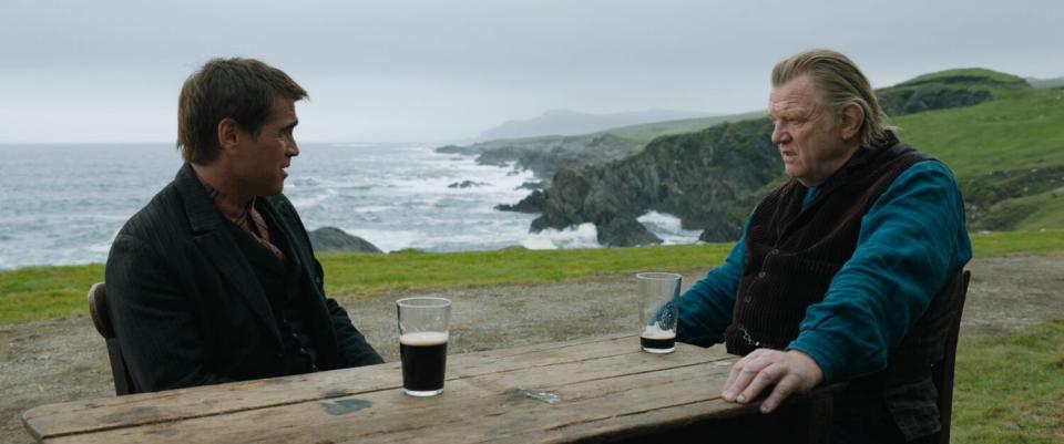 Two men (played by Colin Farrell and Brendan Gleeson) sit at a table outside a seaside Irish pub with pints of beer.