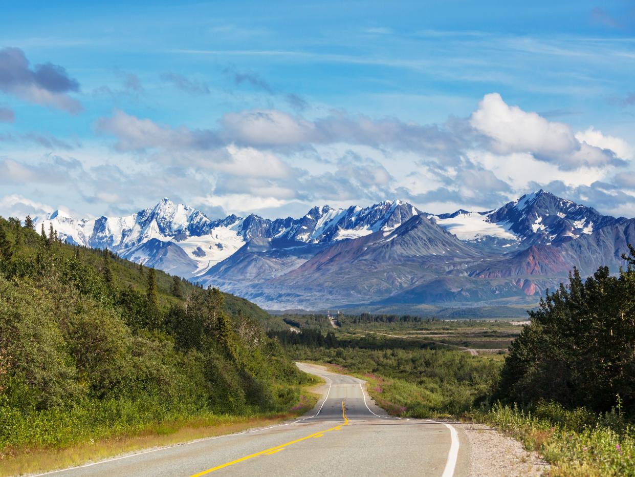 Alaska highway surrounded by green trees heading toward mountains