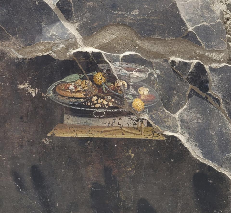 This picture provided on Tuesday, June 27, 2023, by the Pompeii Archaeological Park shows the wall of an ancient Pompeian house with a fresco depicting a table with food. The fresco was found in the atrium of a house in Insula 10 of Regio IX under excavation, to which a bakery was annexed, already partially explored between 1888 and 1891 and whose investigations were resumed last January. (Pompeii Archaeological Park via AP, ho)