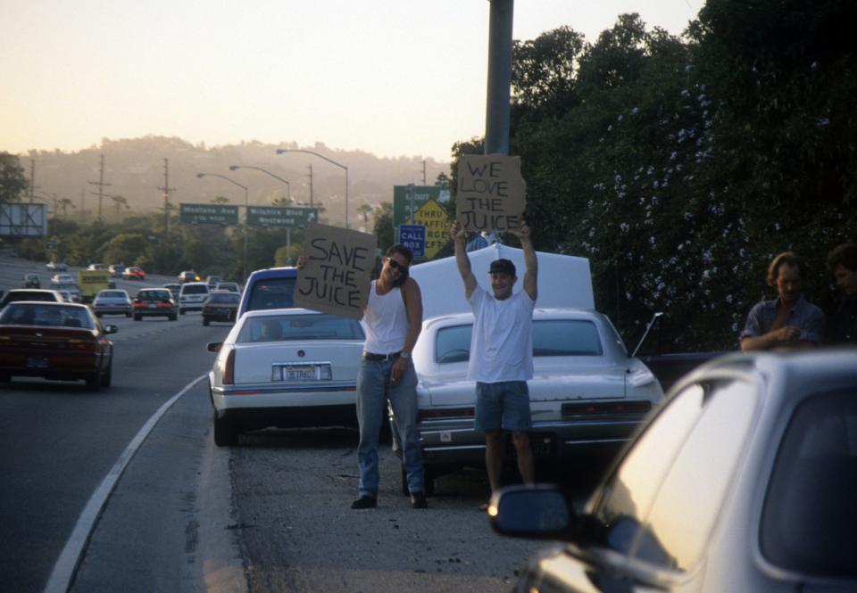 Motorists stand on the side of a highway holding signs that read: Save the Juice and We love the Juice.