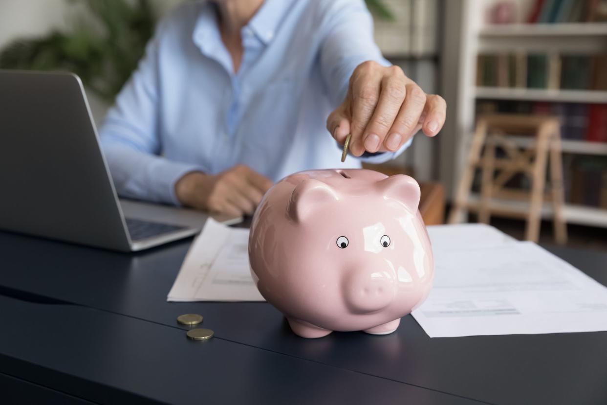 Mature business woman inserting cash into piggy bank. Female accountant, bookkeeper, homeowner saving money, planning budget, making financial reserve. Hand holding coin close up