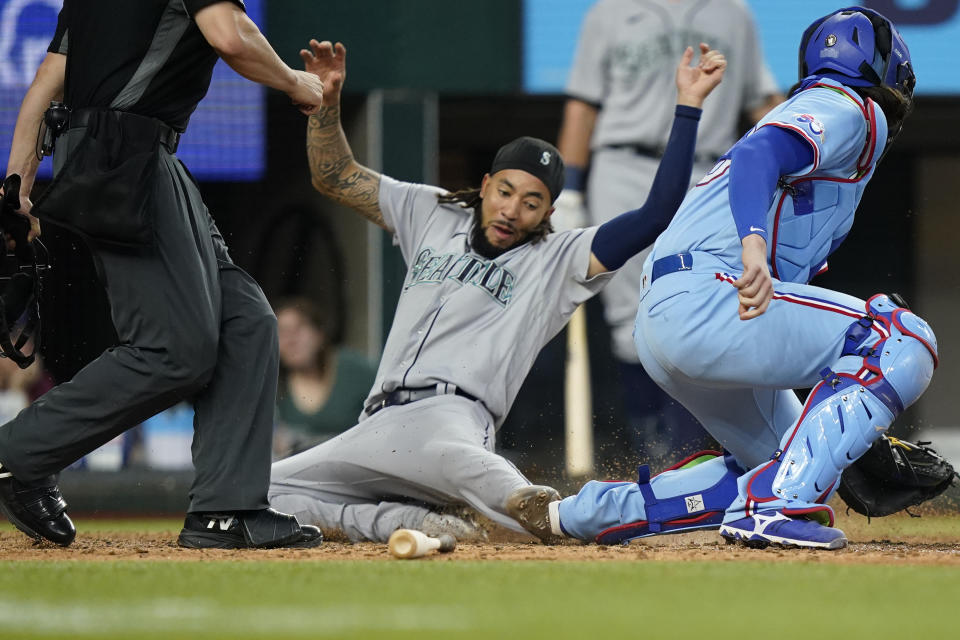 Seattle Mariners' J.P. Crawford, center, slides into home plate scoring against Texas Rangers catcher Jonah Heim, right, on a double by Mariners' Eugenio Suarez during the ninth inning of a baseball game in Arlington, Texas, Sunday, June 5, 2022. (AP Photo/LM Otero)