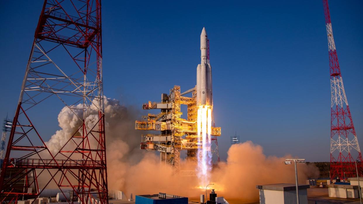  A large white rocket with four smaller boosters lifts off above a plume of fire. 