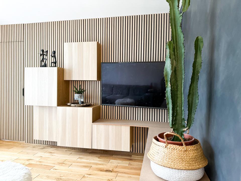 A living room with a wood panelled wall with cabinets fixed to it in a asymmetrical pattern