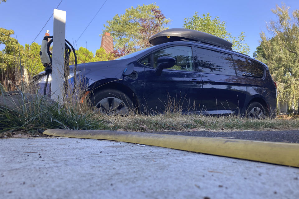 A do-it-yourself electric vehicle charging station for an electric mini-van is seen in the grassy median of this residential street in Portland, Ore., on Sept. 30, 2022 photo. The great transition to electric vehicles is underway for homeowners who can charge their cars in a private garage, but for millions of renters, access to charging remains a significant barrier. (AP Photo/Gillian Flaccus)