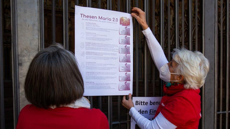 Zwei Aktivistinnen der katholischen Reforminitiative Maria 2.0 hängen ein Plakat mit ihren Thesen an das Hauptportal des Freiburger Münsters.