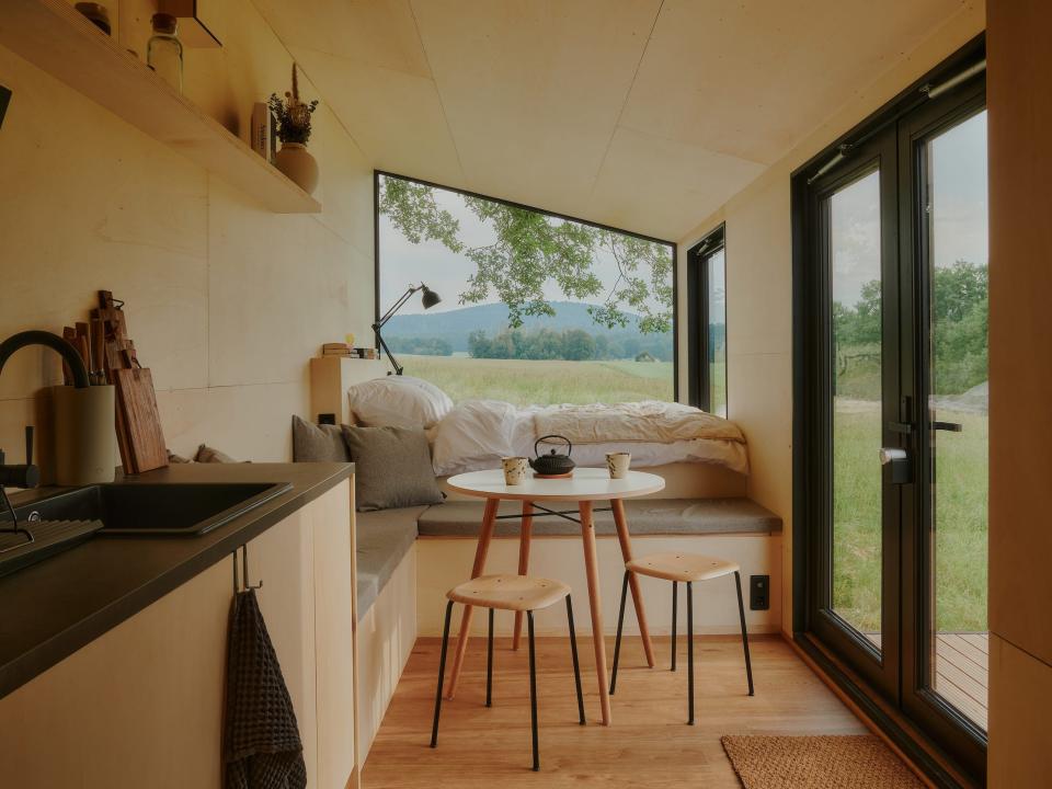 A look inside a Raus cabin with a bed, dining table, kitchen, windows with views of nature.