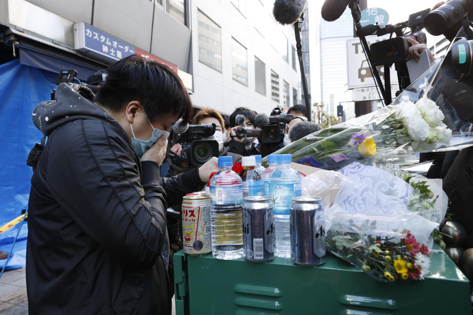 A mourner offers a flower near a building where a fire broke out in Osaka, western Japan Saturday, Dec. 18, 2021. A fire that spread from a fourth-floor mental clinic in the eight-story building in downtown Osaka on Friday left more than 20 dead in what police were investigating as a possible case of arson and murder. (Yukie Nishizawa/Kyodo News via AP)