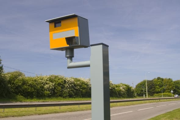 Landscape photo of road and yellow speeding camera.