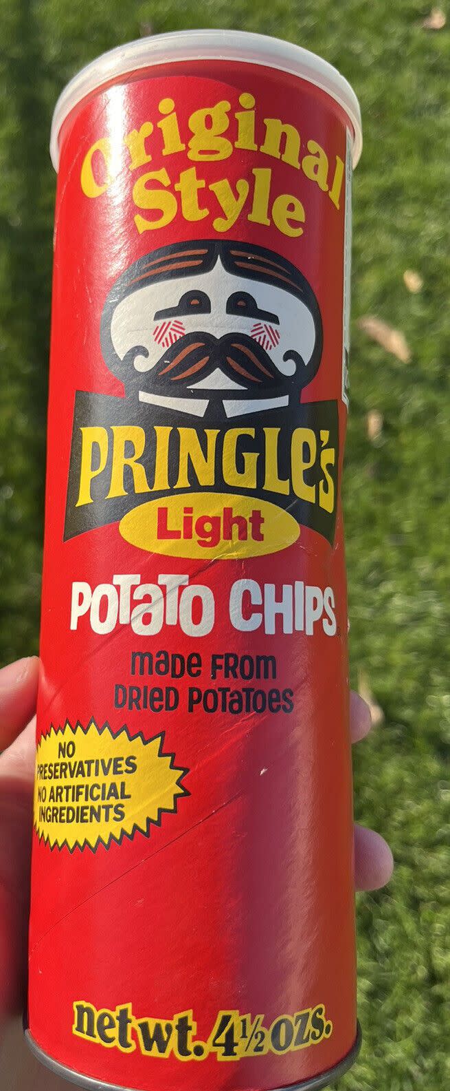 1970's vintage original style Pringles Light potato chips can 4.5 oz., left hand holding the red can, grass blurred in the background