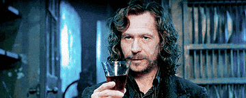 Gary Oldman winks at someone before drinking wine