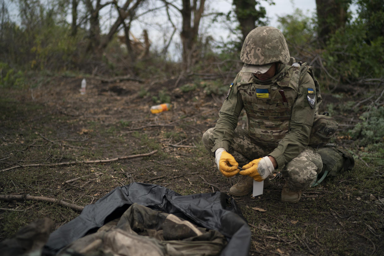 A Ukrainian serviceman identifies the body of a Ukrainian soldier in a retaken area near the border with Russia in Kharkiv region, Ukraine, Saturday, Sept. 17, 2022. (AP Photo/Leo Correa)