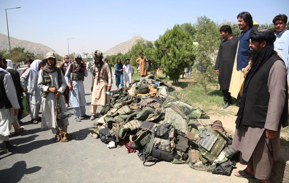 Taliban fighters stand beside the belongings of Afghan security soldiers in Kabul
