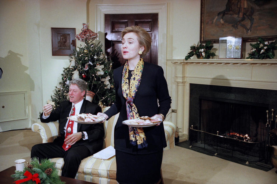 FILE - First lady Hillary Clinton offers cookies to the Arkansas press corps during an interview with President Bill Clinton in the Roosevelt Room at the White House, Washington, Dec. 22, 1993. In pre-pandemic times, presidents and first ladies spent many evenings in December before Christmas hosting nearly two dozen holiday parties and receptions, sometimes two per day, where they stood in line for hours to pose for photos with ecstatic guests. (AP Photo/J. Scott Applewhite, File)