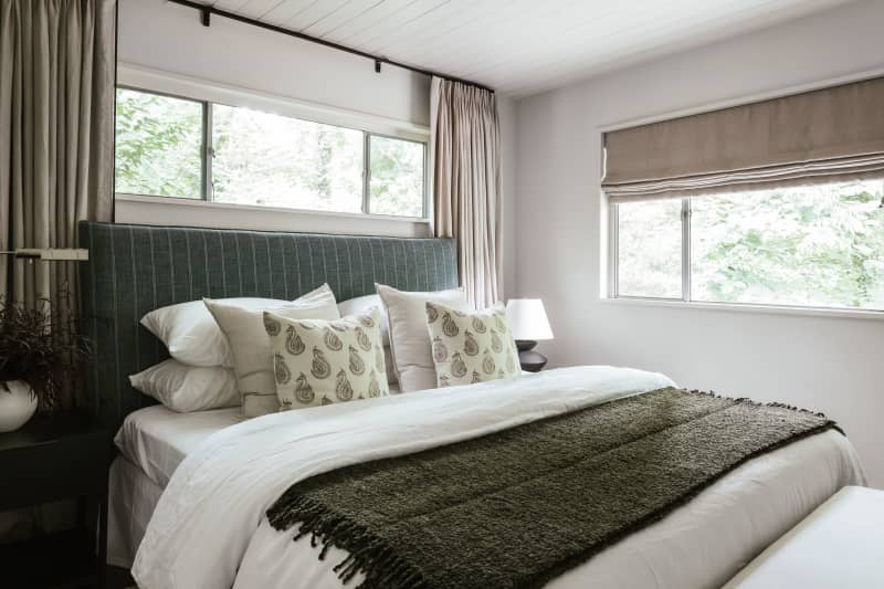 Tongue and groove paneling on ceiling, dark teal fabric headboard, white linens, dark gray throw blanket, round vintage lighting fixture