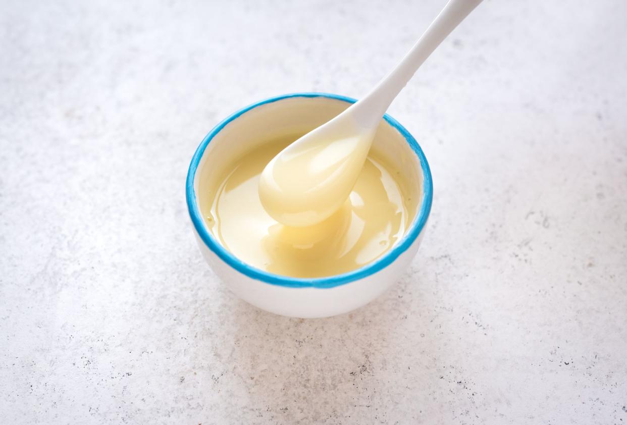 Condensed milk pouring in white bowl. Sweet vanilla sauce, condensed or evaporated milk, top view, copy space.