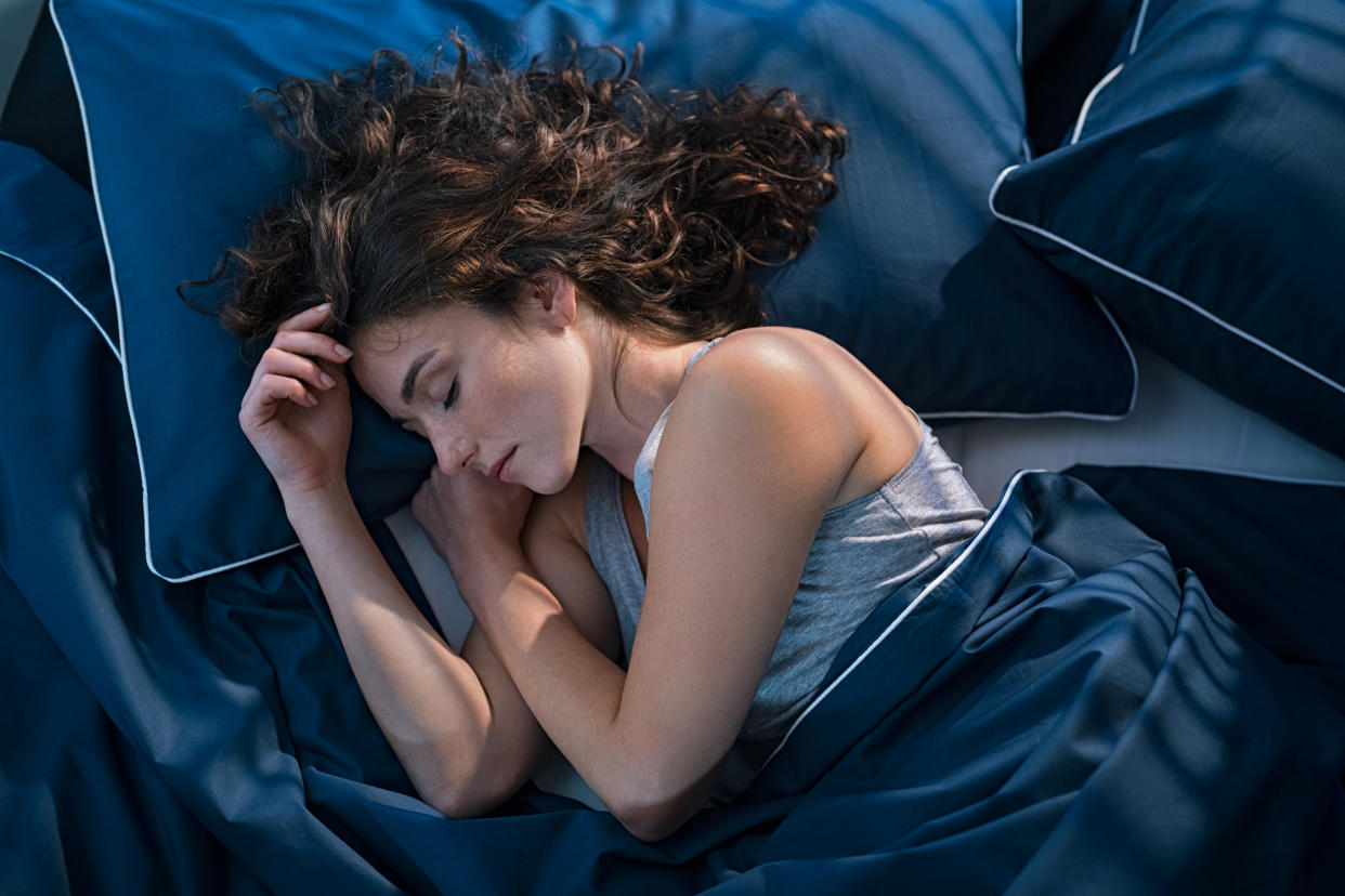 Top view of young woman sleeping on side in her bed at night. Beautiful girl sleeping profoundly and dreaming at home with blue blanket. High angle view of woman asleep with closed eyes.