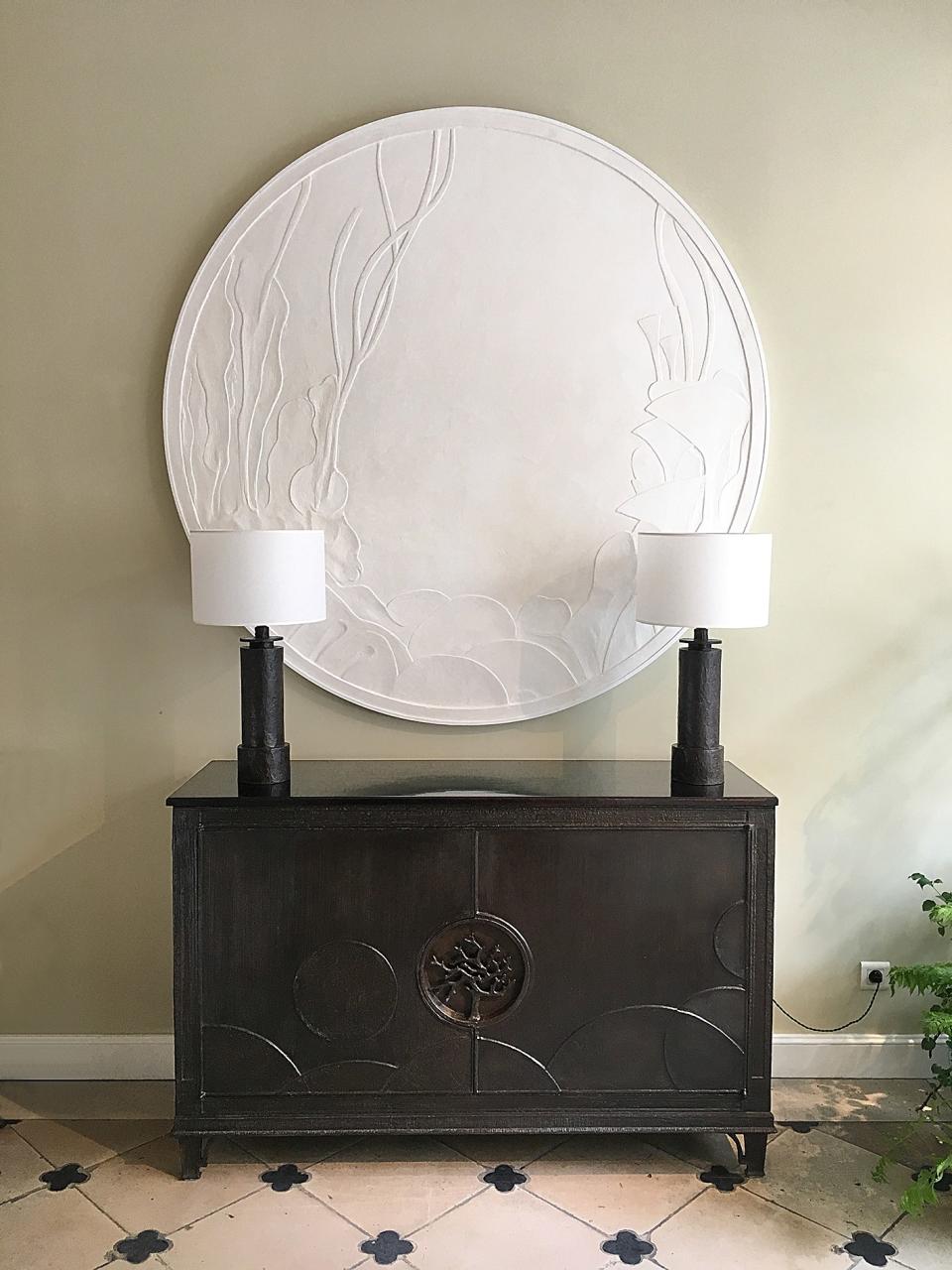 A pair of bronze lamps frame a plaster bas relief at the gallery.